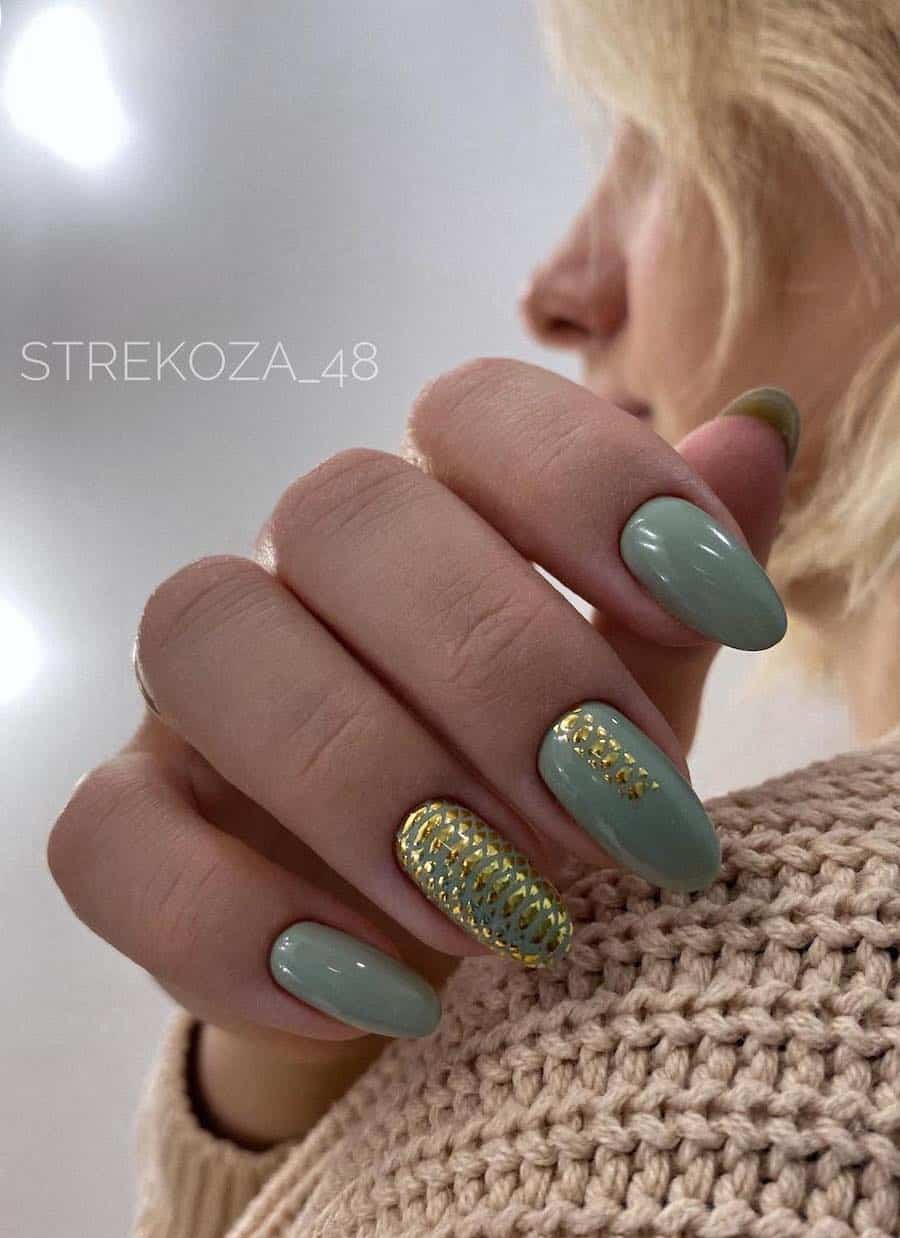 A hand with medium almond nails painted a glossy sage green with gold scale details