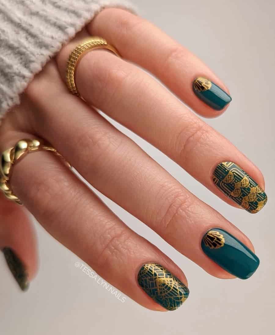 A hand with short squoval nails painted a dark green with gold art deco details