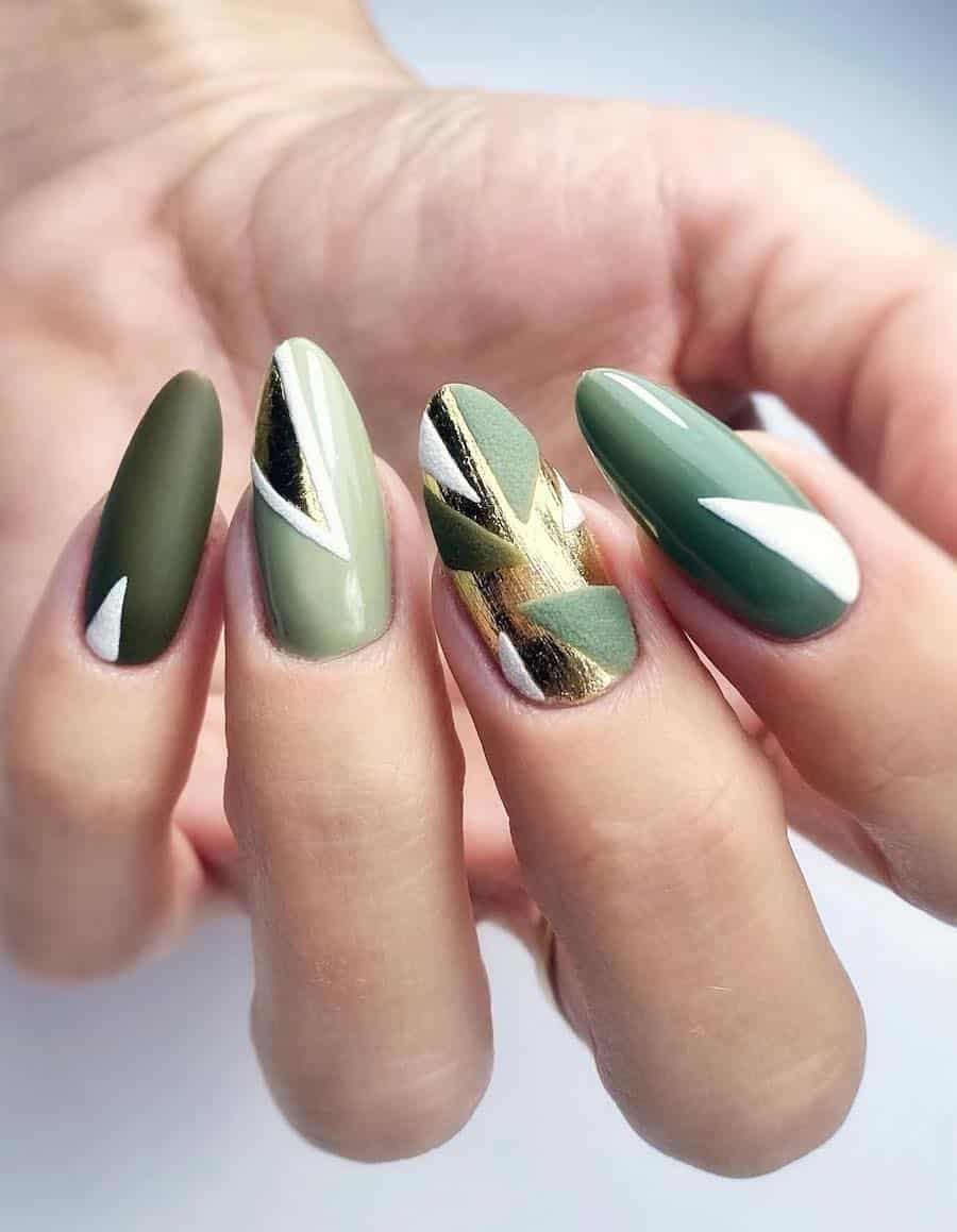 A hand with long almond nails painted in a geometric pattern with shades of green, white, and shimmering gold polish