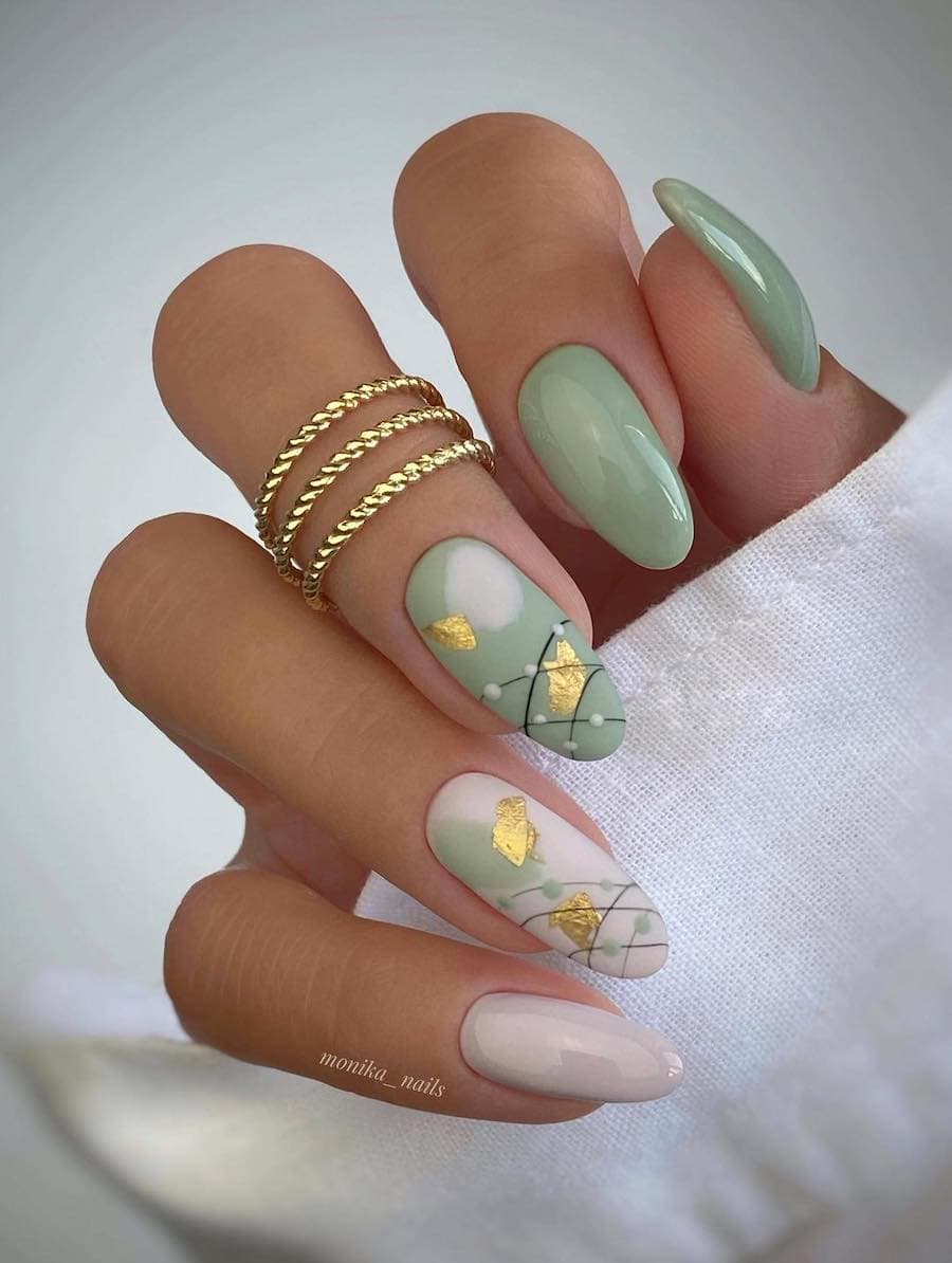 A hand with long almond nails painted a glossy spring green with cream accent nails, gold foil, and black line details