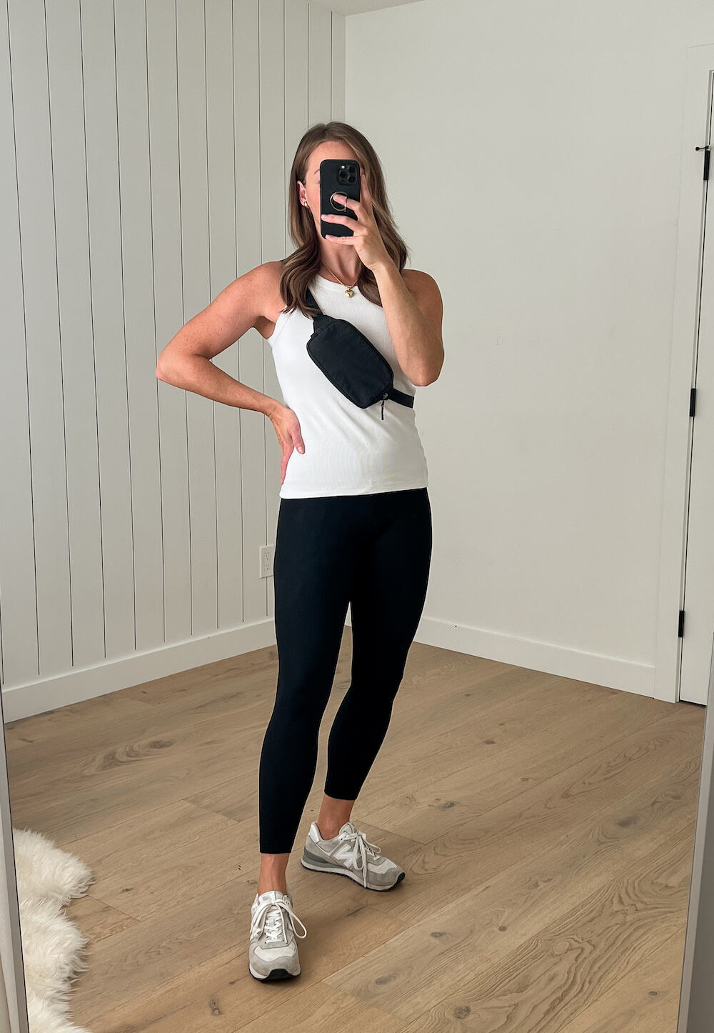 Christal wearing a white tank top, black leggings, white sneakers, and a black Lululemon belt bag crossbody style