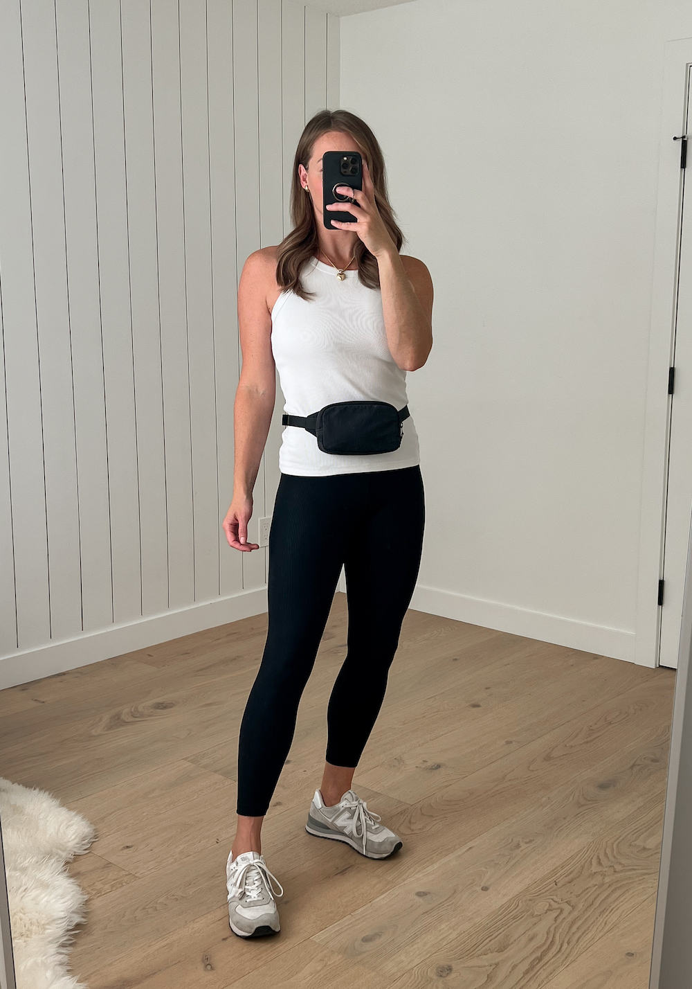 Christal wearing a white tank top, black leggings, white sneakers, and a black Lululemon belt bag high at the true waistline