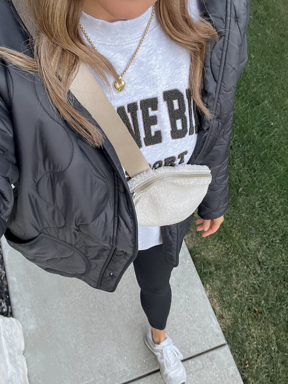 Up close shot of a woman wearing leggings, sneakers, a sweatshirt and a puffer jacket with a Lululemon belt bag.