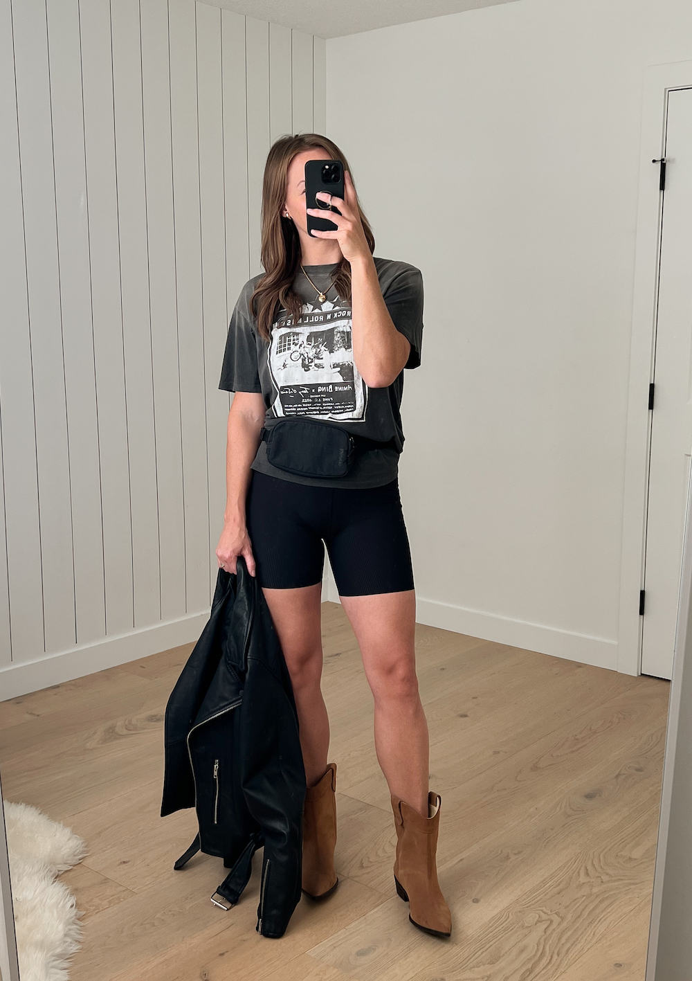 Woman wearing biker shorts and a graphic tee with western boots and a Lululemon belt bag.