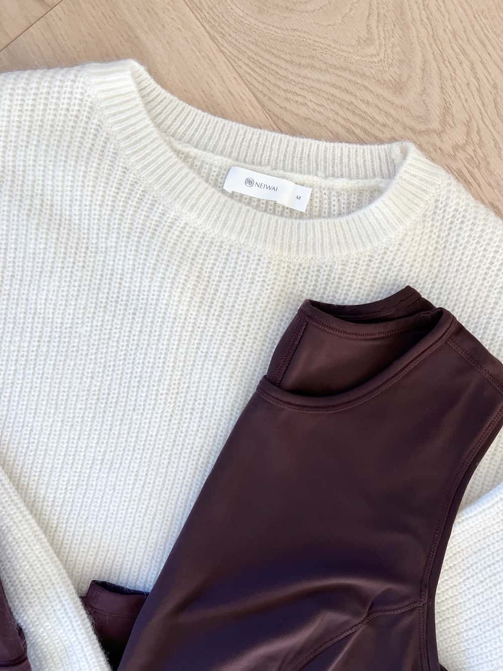 Close up flat lay view of a Neiwai knit ivory sweater and dark brown activewear tank top 