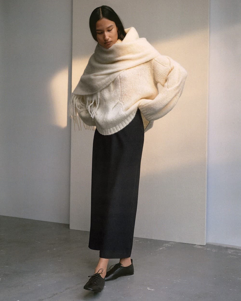 woman wearing an oversized ivory sweater and scarf with a black maxi skirt from Arket
