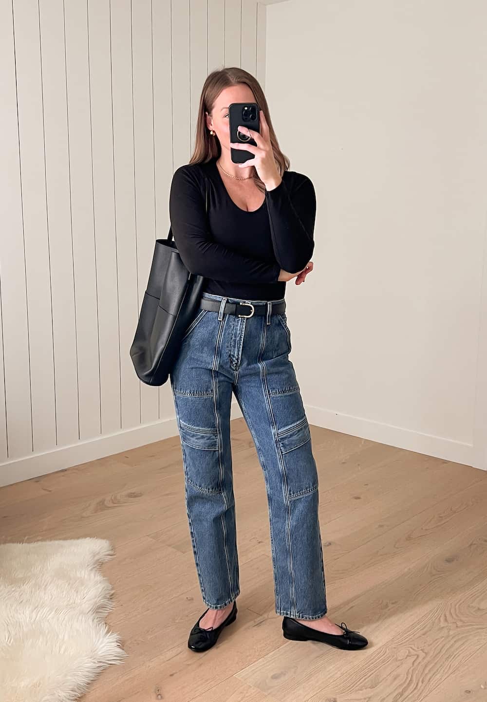 Christal wearing a black long-sleeved top with blue cargo jeans and black ballet flats and an Oak & Fort faux leather tote bag