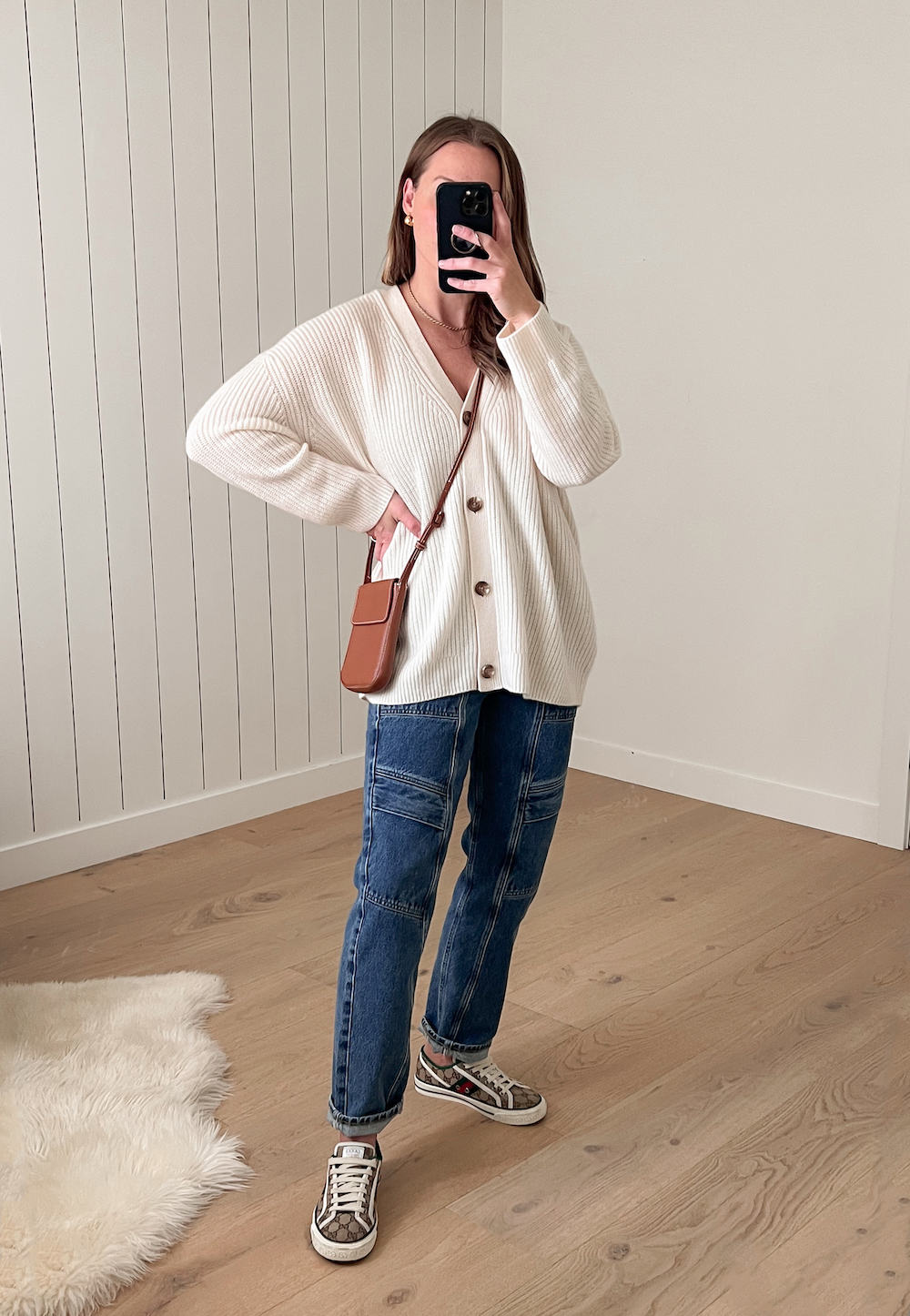 Christal wearing an ivory knit oversized cardigan from Quince (a brand like Everlane) with blue cargo jeans and tan canvas sneakers 