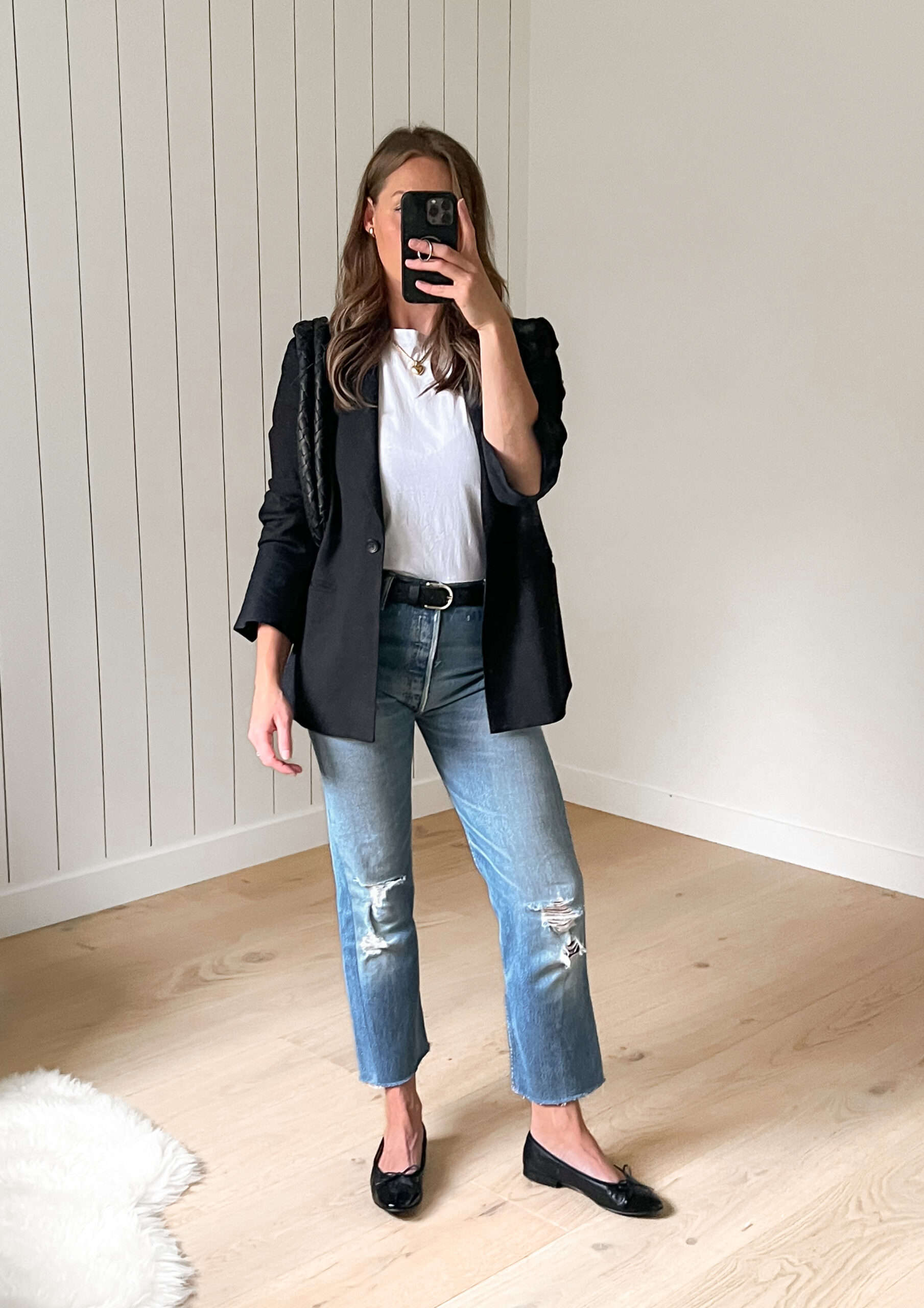 Woman wearing distressed straight jeans with a white t-shirt under a black blazer and ballet flats.