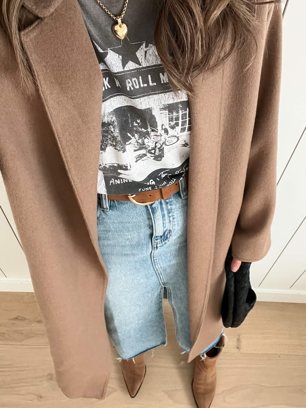 Up close shot of a woman wearing a denim maxi shirt, brown western style boots, a graphic tee and a brown trench coat.