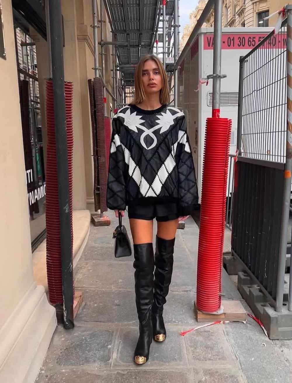Woman wearing a black and white western style long sleeve shirt with black shorts and black over the knee boots.