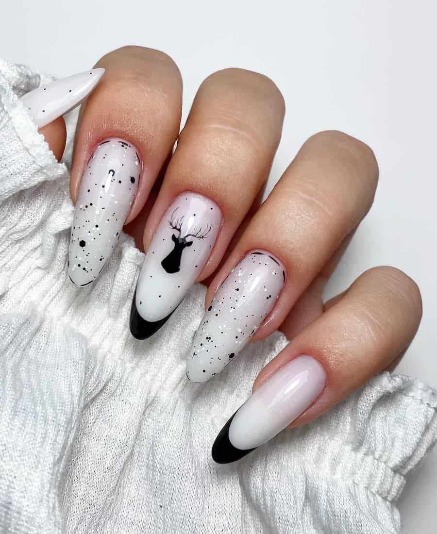 A hand with long almond nails painted a milky white with black nail art including French tips, speckled details, and reindeer nail art