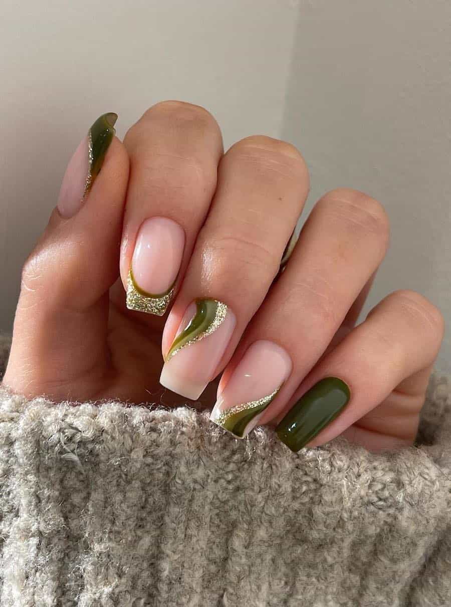 A hand with medium nude square nails with gold and green waves and French tips with one solid-colored accent nail