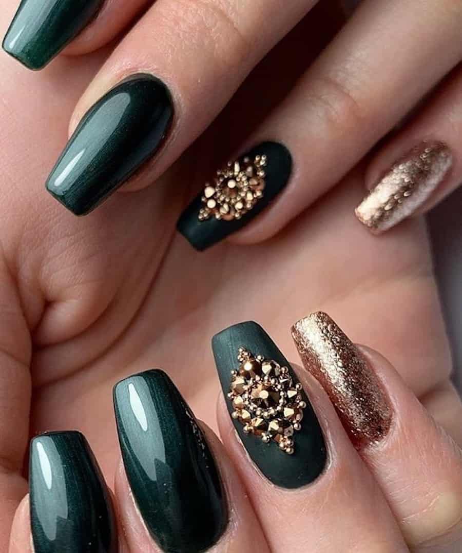 A hand with medium coffin nails painted a glossy dark green with accent nails featuring sparkly gold polish and matte green polish with gold gems