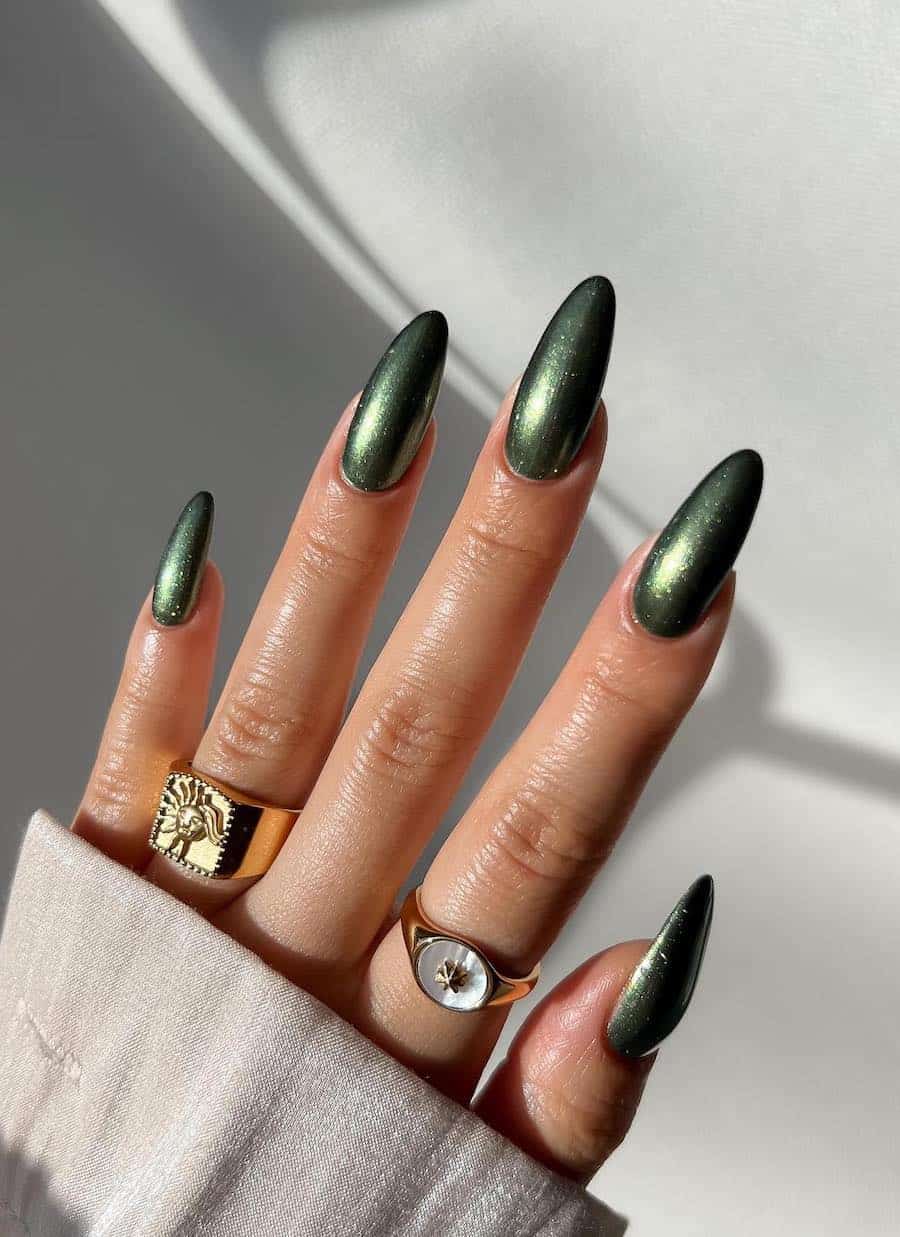 A hand with long almond nails painted a metallic moss green with a gold chrome finish