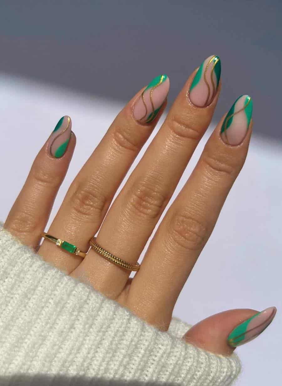 A hand with medium almond nails painted a glossy nude pink with green waves and wavy gold lines