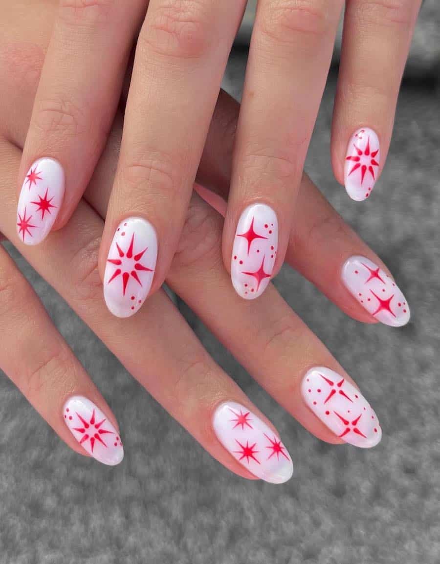 A hand with short milky white almond nails with red stars and sparkles