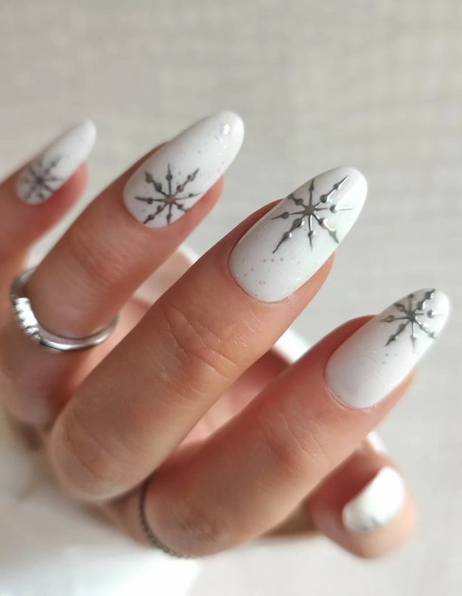 A hand with medium white almond nails with white glitter and silver snowflakes