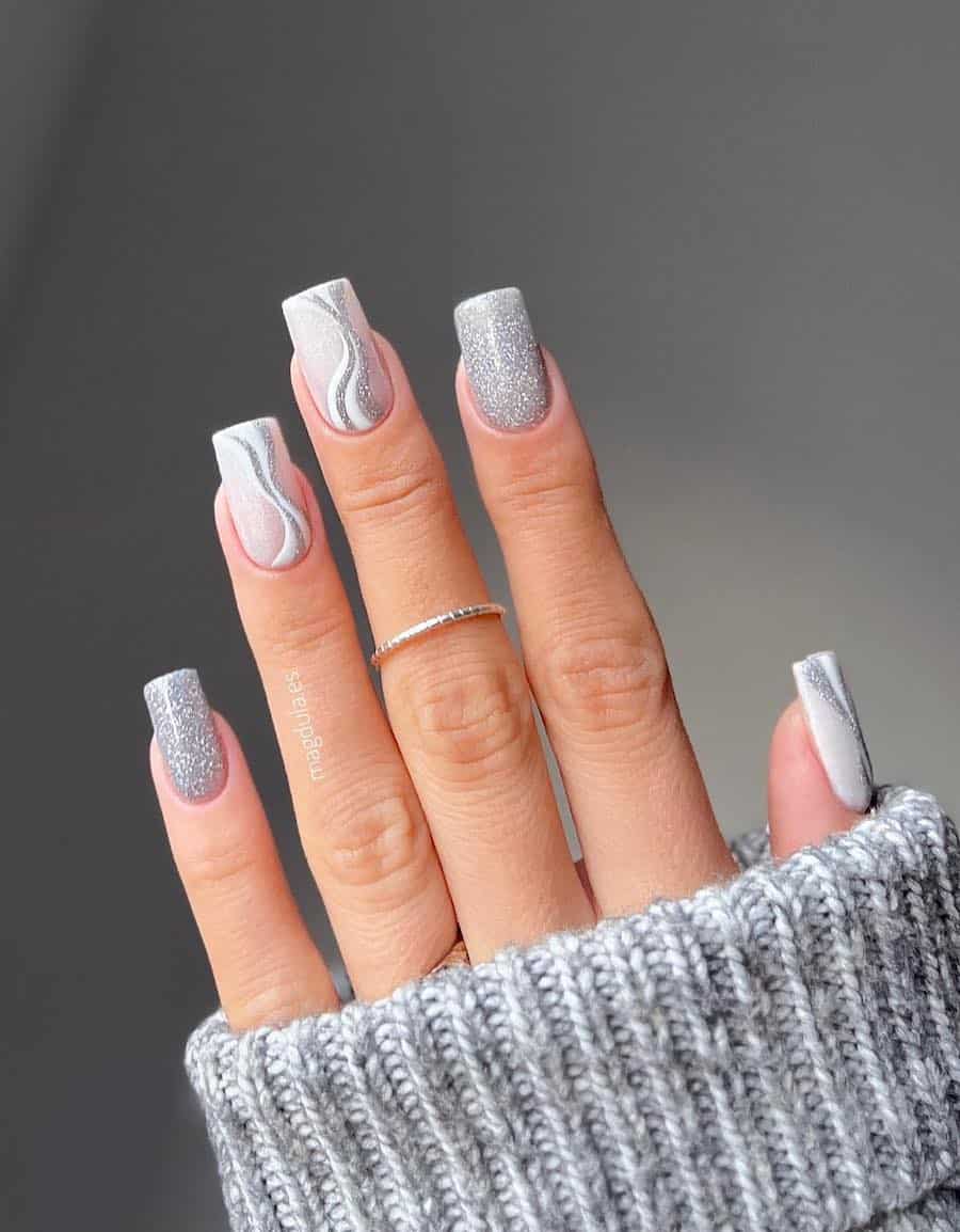 A hand with medium square nails painted with a silver glitter polish and accent nails with white and silver waves