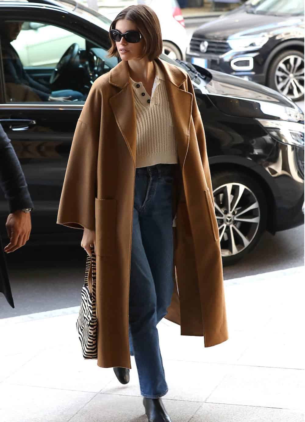 Off-duty model Kaia Gerber wearing jeans, a cropped sweater and a camel colored trench coat.
