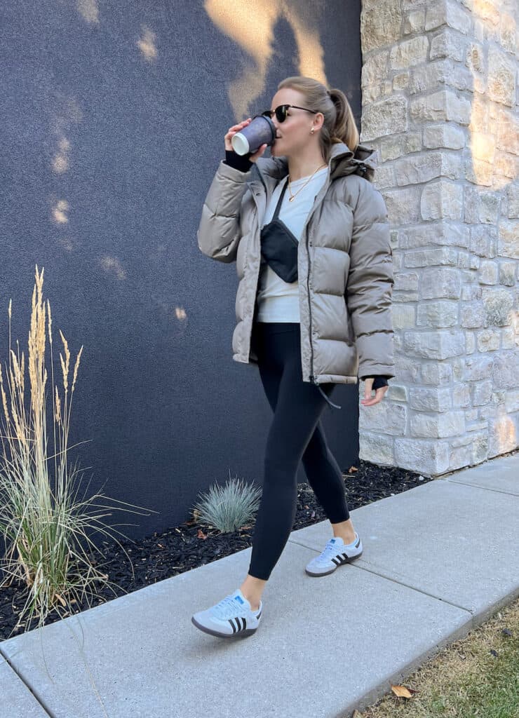 woman wearing an Aritzia Super Puff dupe jacket in taupe with a white top, black leggings and white sneakers