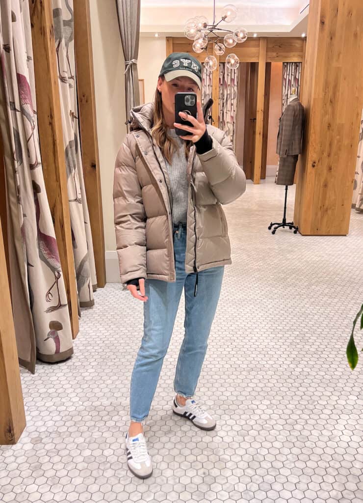 woman wearing the Aritzia Super Puff jacket in taupe with blue jeans and white sneakers
