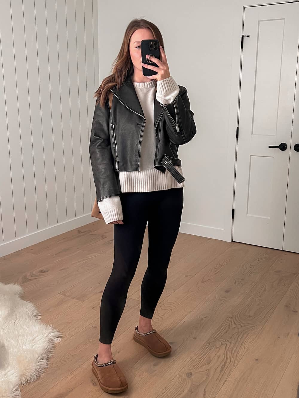 woman wearing a distressed leather jacket over a long oversized turtleneck sweater, black leggings, and Ugg Tasman slippers