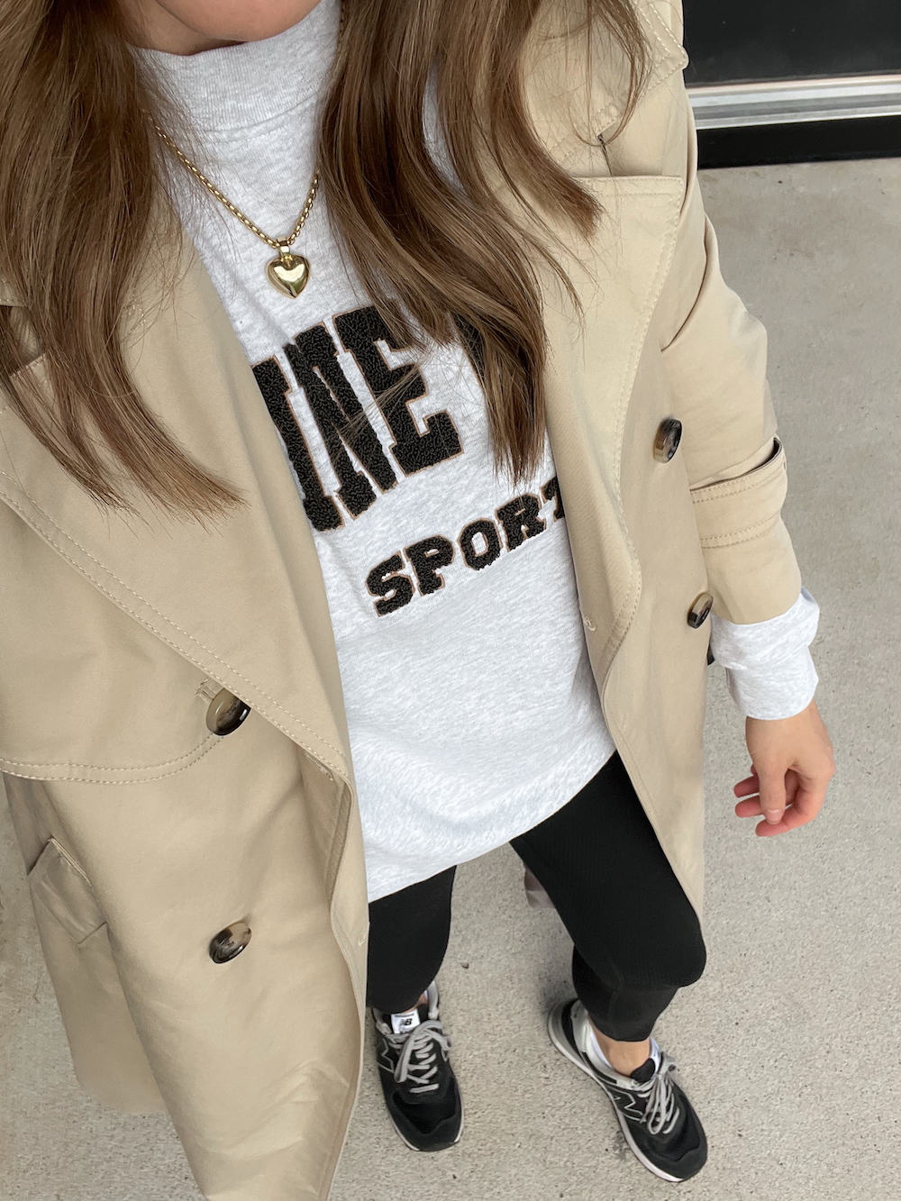 overhead view of a woman wearing a casual leggings outfit with black leggings, black sneakers, a grey sweatshirt, and a tan trench coat