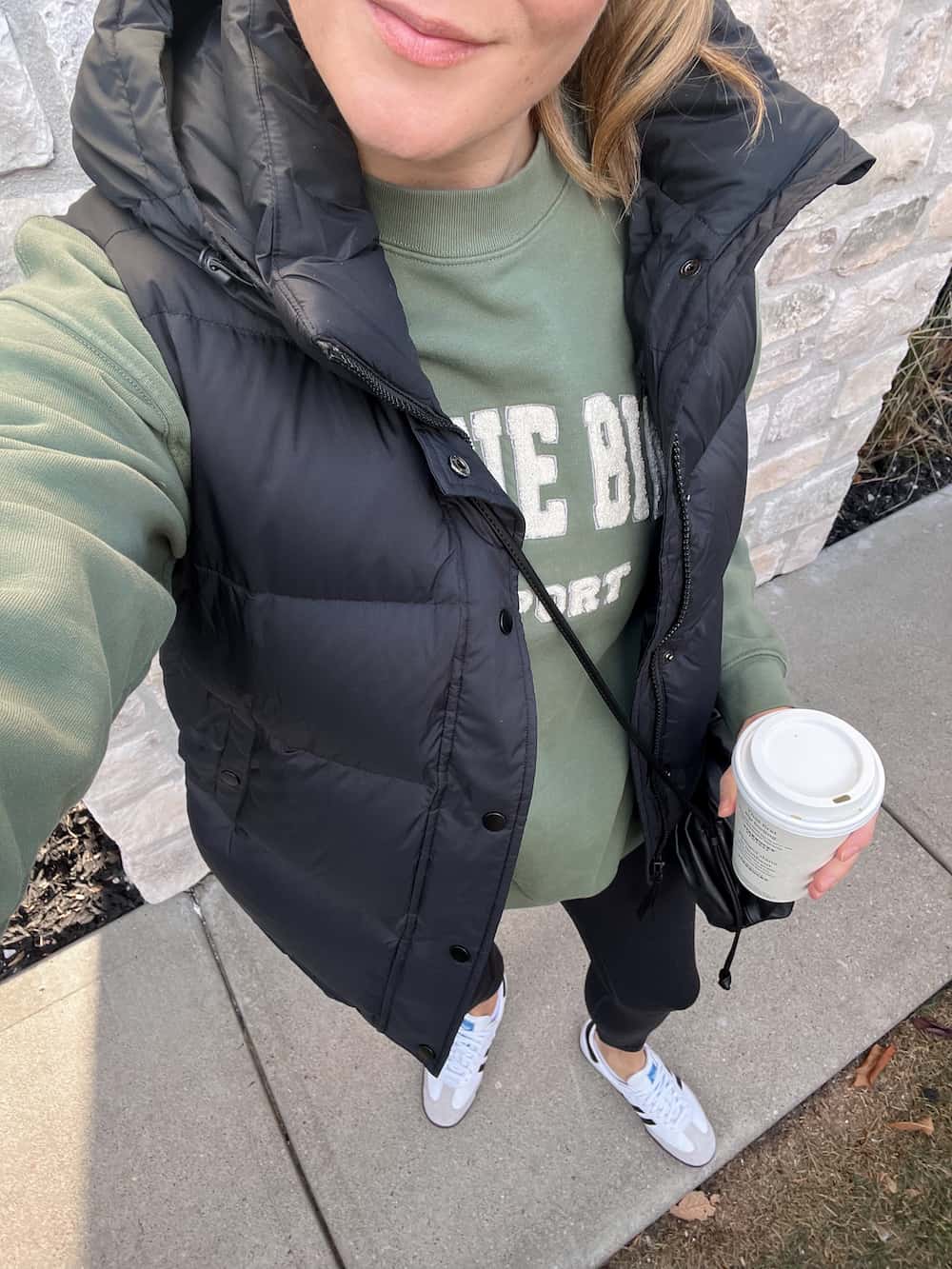 overhead view of a woman wearing a black puffer vest with a green sweatshirt, black leggings, and white sneakers