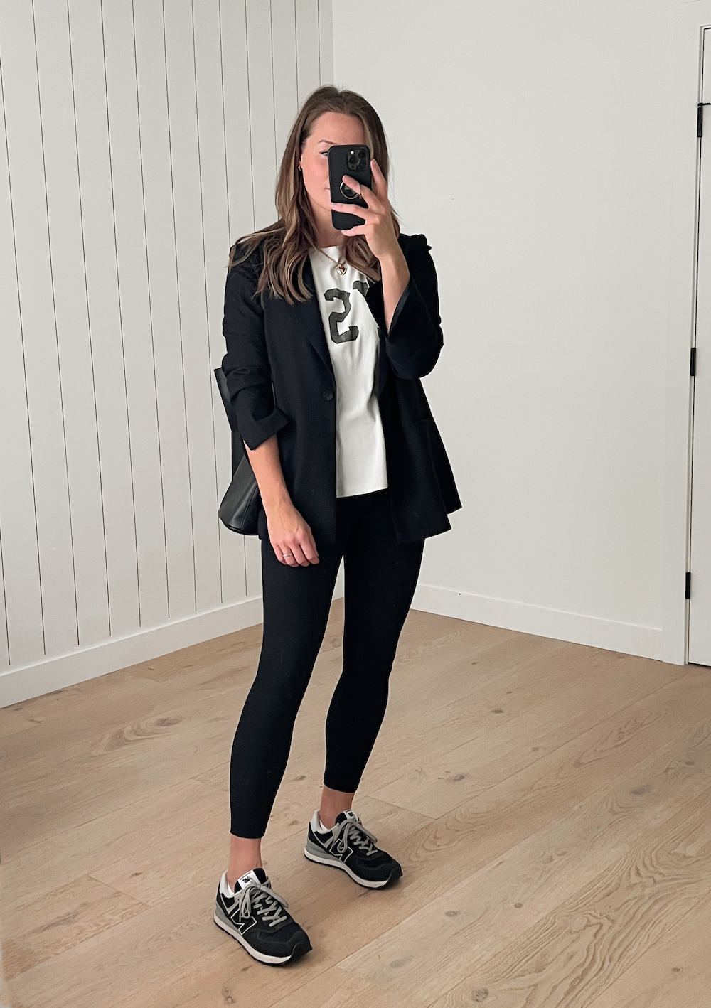 Woman wearing an oversized black blazer over a white t-shirt with black leggings and black sneakers