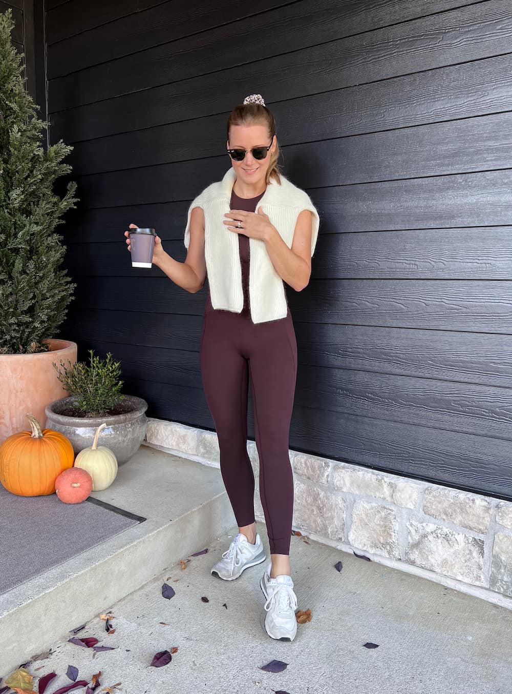 woman wearing a casual outfit with brown leggings and a matching brown tank top, white sneakers, and a white knit sweater over her shoulders