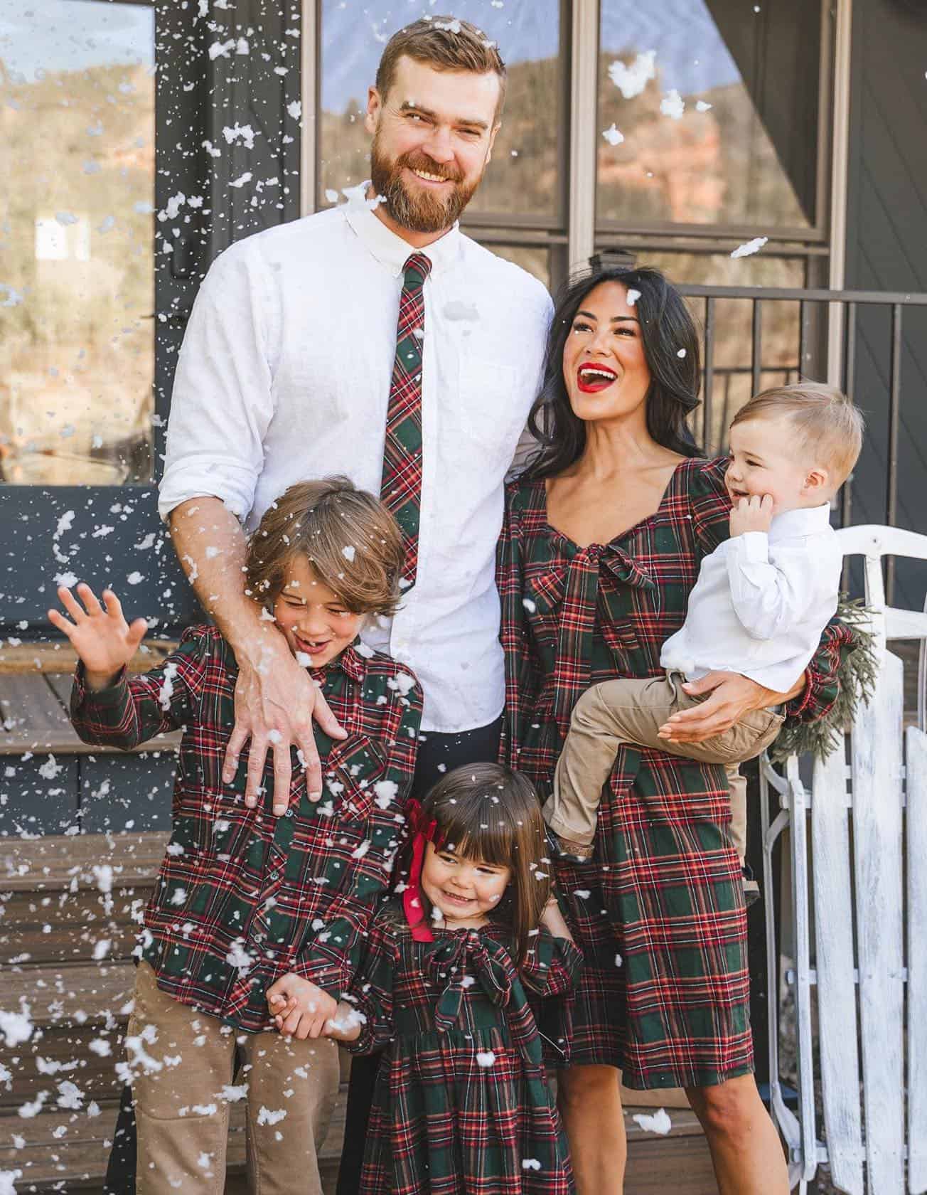 A winter family photoshoot with a family of five wearing red and green plaid and white
