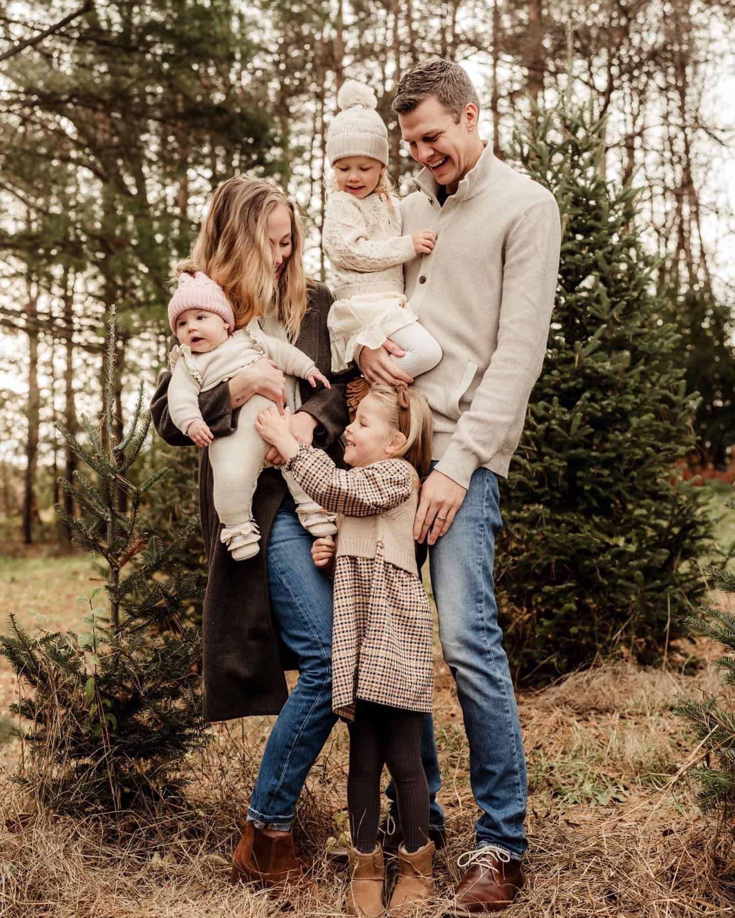 A winter family photoshoot with a family of five wearing neutral colors like white, brown, and beige with pops of denim blue