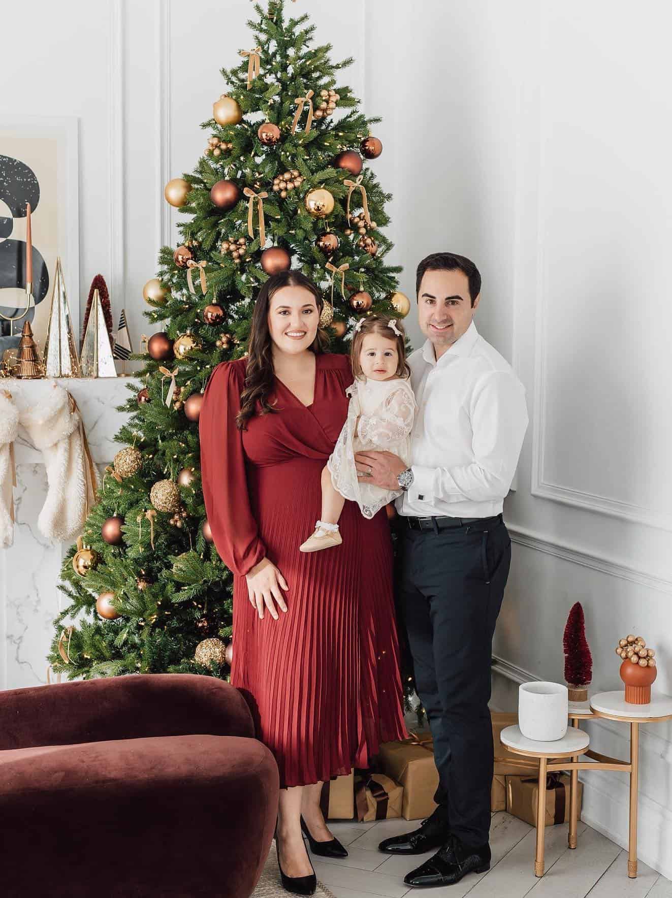A Christmas family photo with a family of three wearing dressy red, white, and black pieces