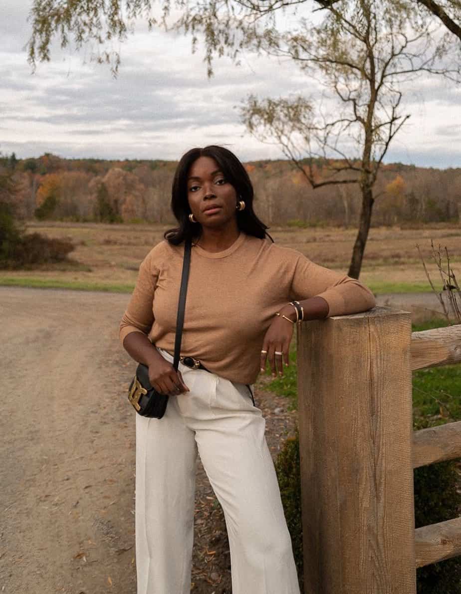 Black woman wearing a camel long-sleeve sweater with a black belt and cream pleated trousers