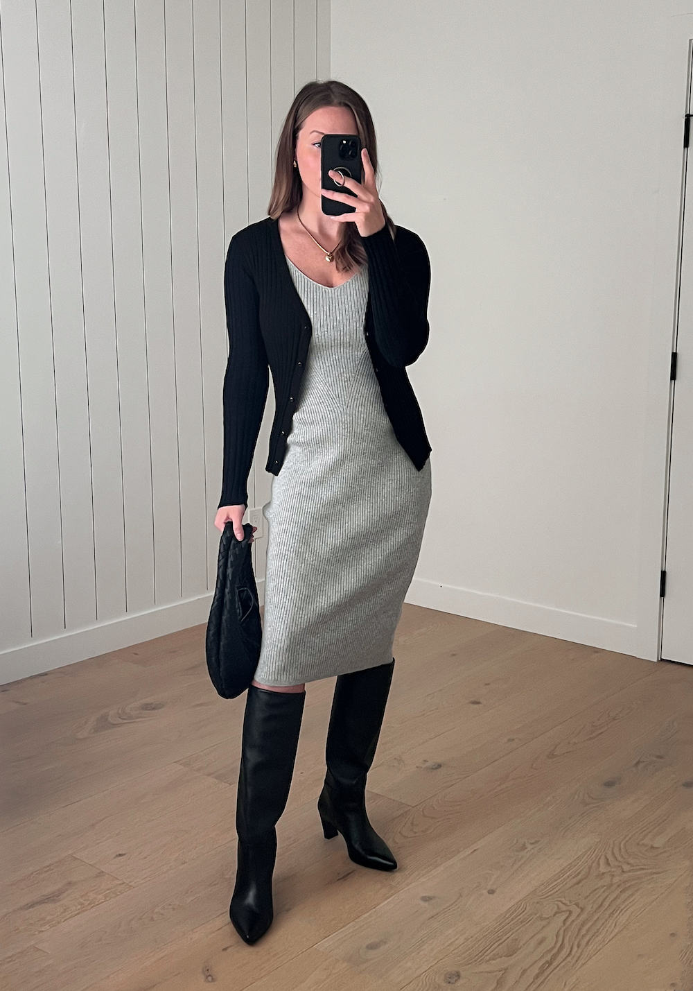 Christal wearing a grey sweater dress and a black cardigan with tall black boots.