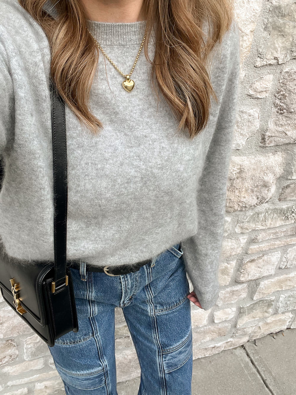 close up of a woman wearing a grey fuzzy cashmere Lilysilk pullover sweater with blue cargo jeans and a black YSL purse