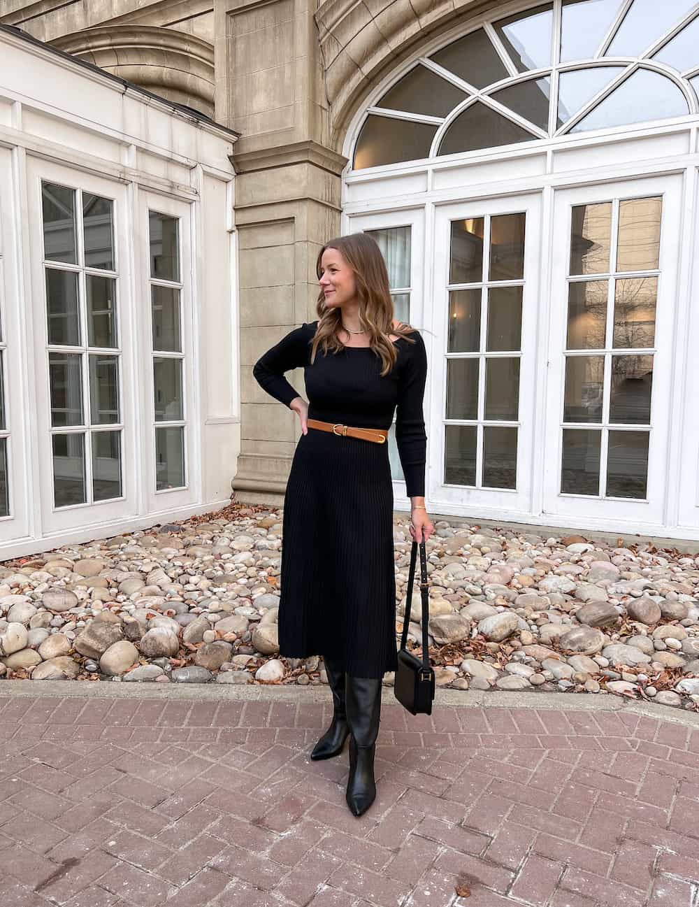 woman wearing a black knit midi dress from Lilysilk with black knee high boots and a brown belt at the waist