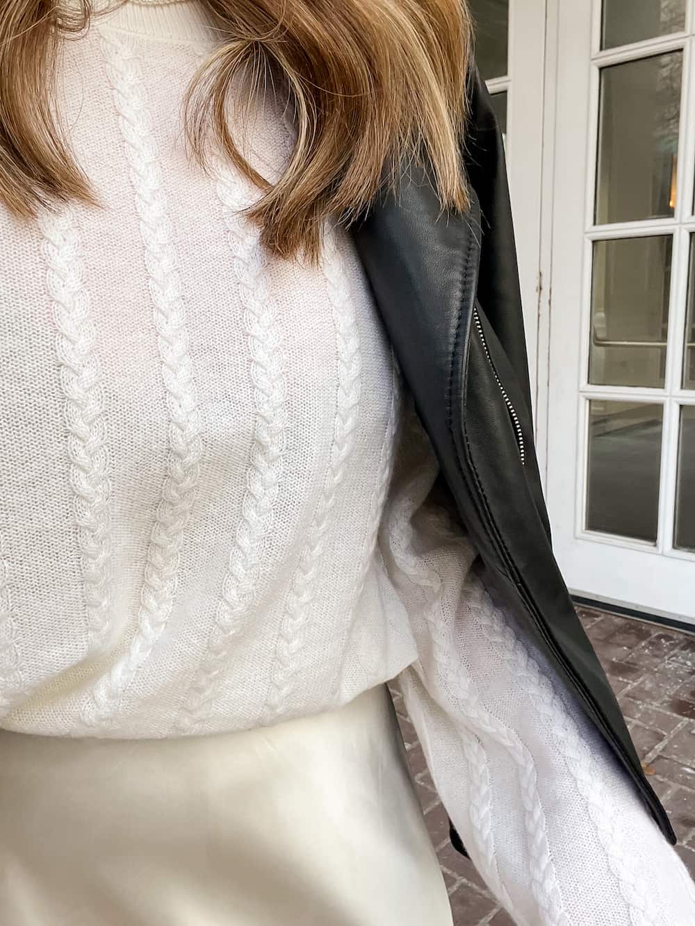 close up of a woman wearing a holiday outfit with a leather jacket over a Lilysilk ivory cable knit sweater, and an ivory slip skirt