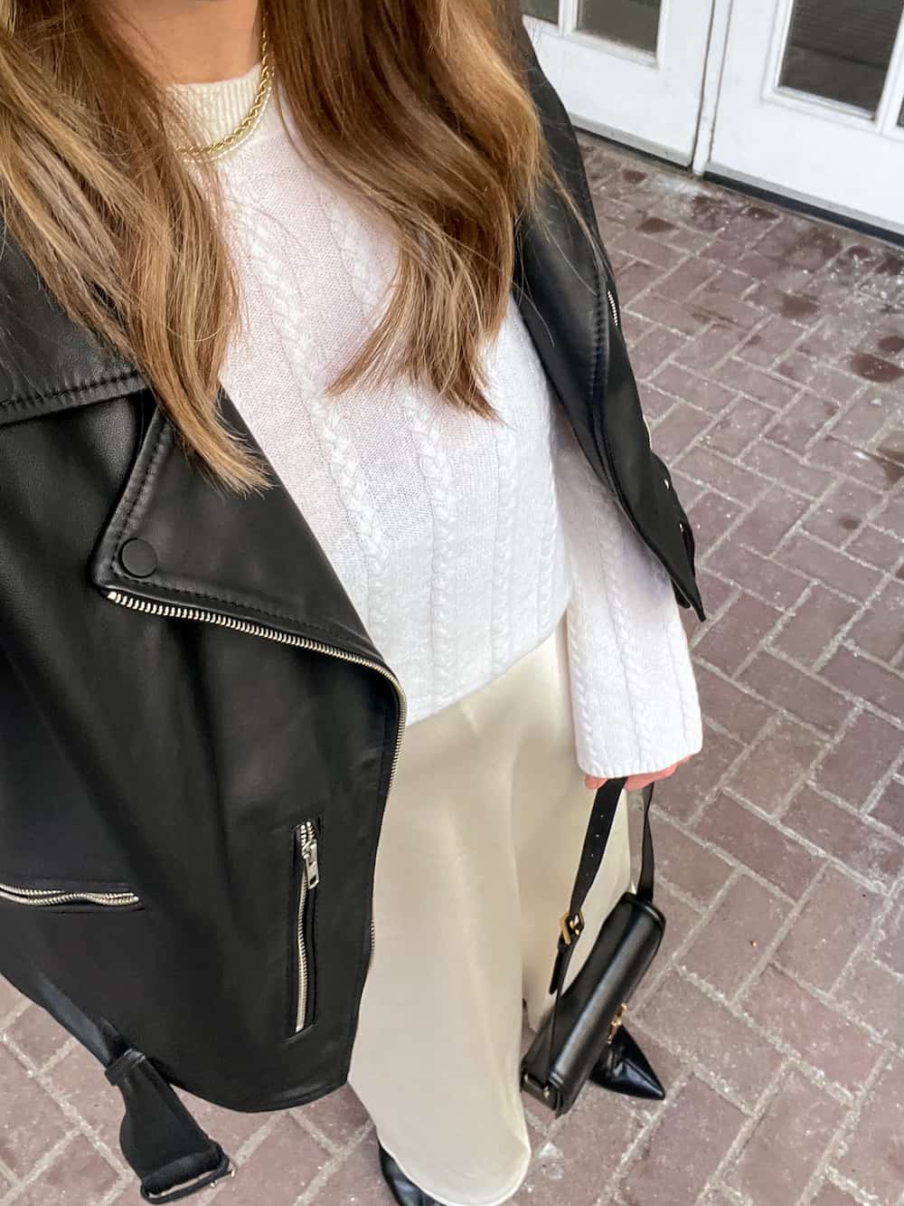 close up of a woman wearing a holiday outfit with a leather jacket over a Lilysilk ivory cable knit sweater, and an ivory slip skirt and black ankle boots