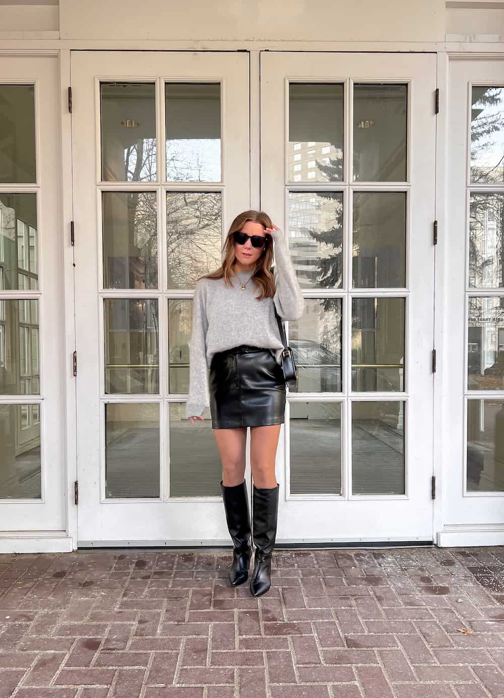 woman wearing a grey fuzzy cashmere Lilysilk pullover sweater with a black leather mini skirt and black knee-high boots for a holiday outfit