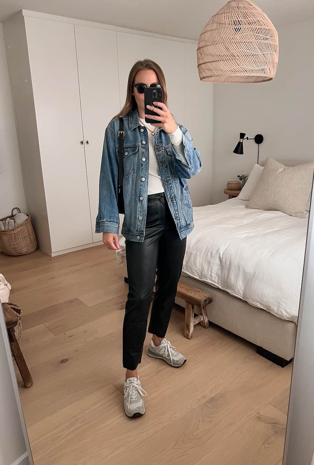 woman wearing an oversized denim jacket with black leather pants and white New Balance 547 sneakers