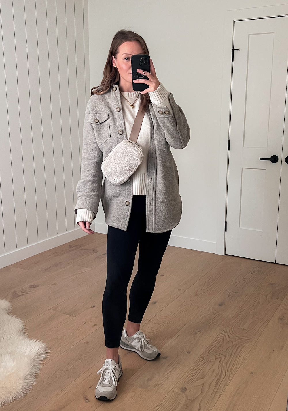 woman wearing a taupe shirt jacket over an ivory sweater with black leggings and white New Balance 574 sneakers