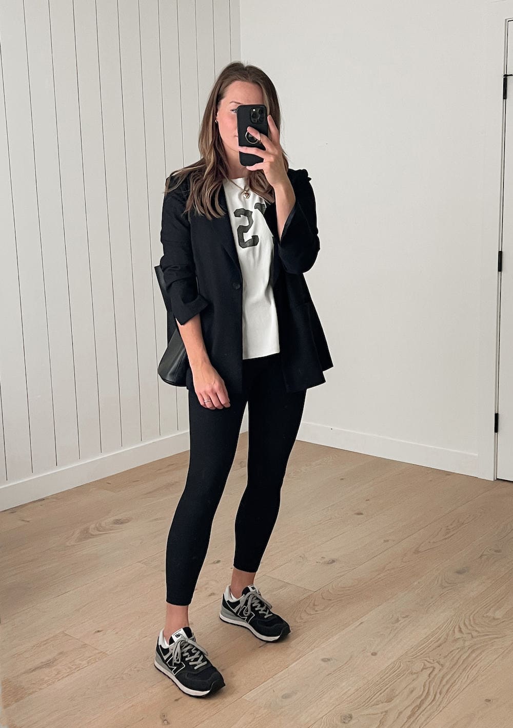 Woman wearing an oversized black blazer over a white t-shirt with black leggings and black New Balance 574 sneakers