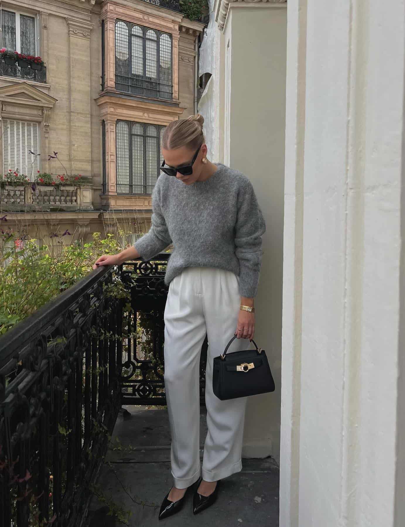 woman wearing an elegant outfit with a grey cashmere sweater, ivory trousers, and black accessories 