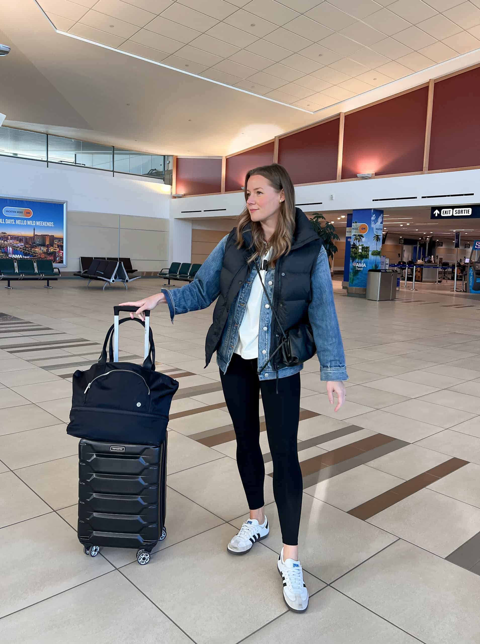 Christal wearing black leggings, a white t-shirt, a denim jacket and a black puffer vest with sneakers at the airport.
