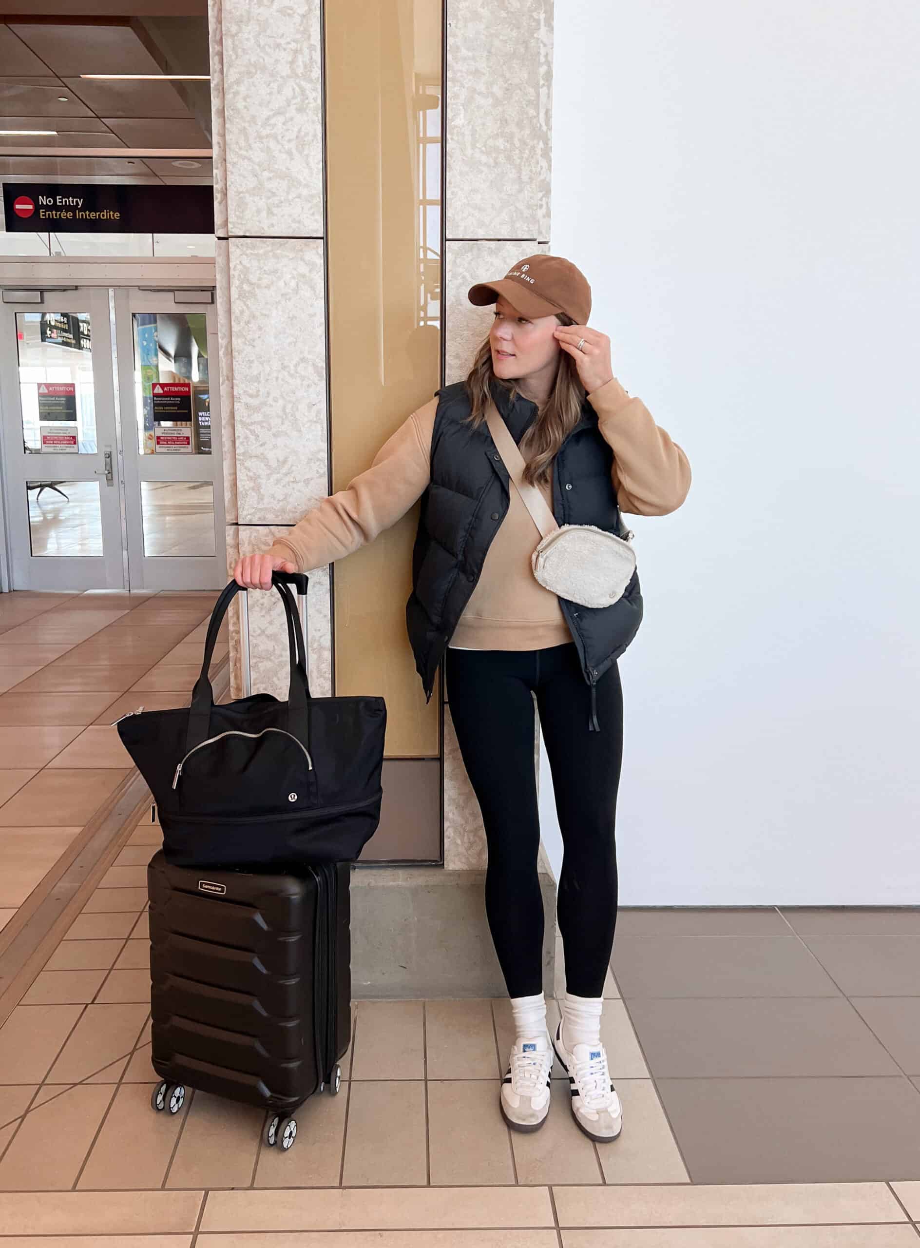Christal wearing black leggings, a tan sweatshirt and a black puffer vest in the airport.