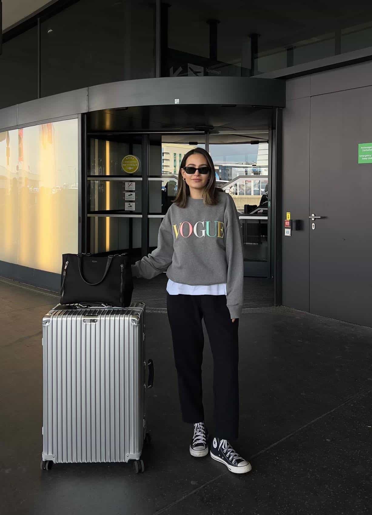 Woman wearing black sweat pants and a vogue sweatshirt with high top sneakers in the airport.