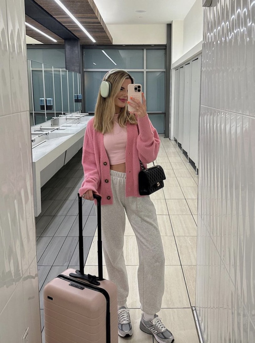 Woman wearing grey sweatpants, a pink cropped top and a pink cardigan in the airport.