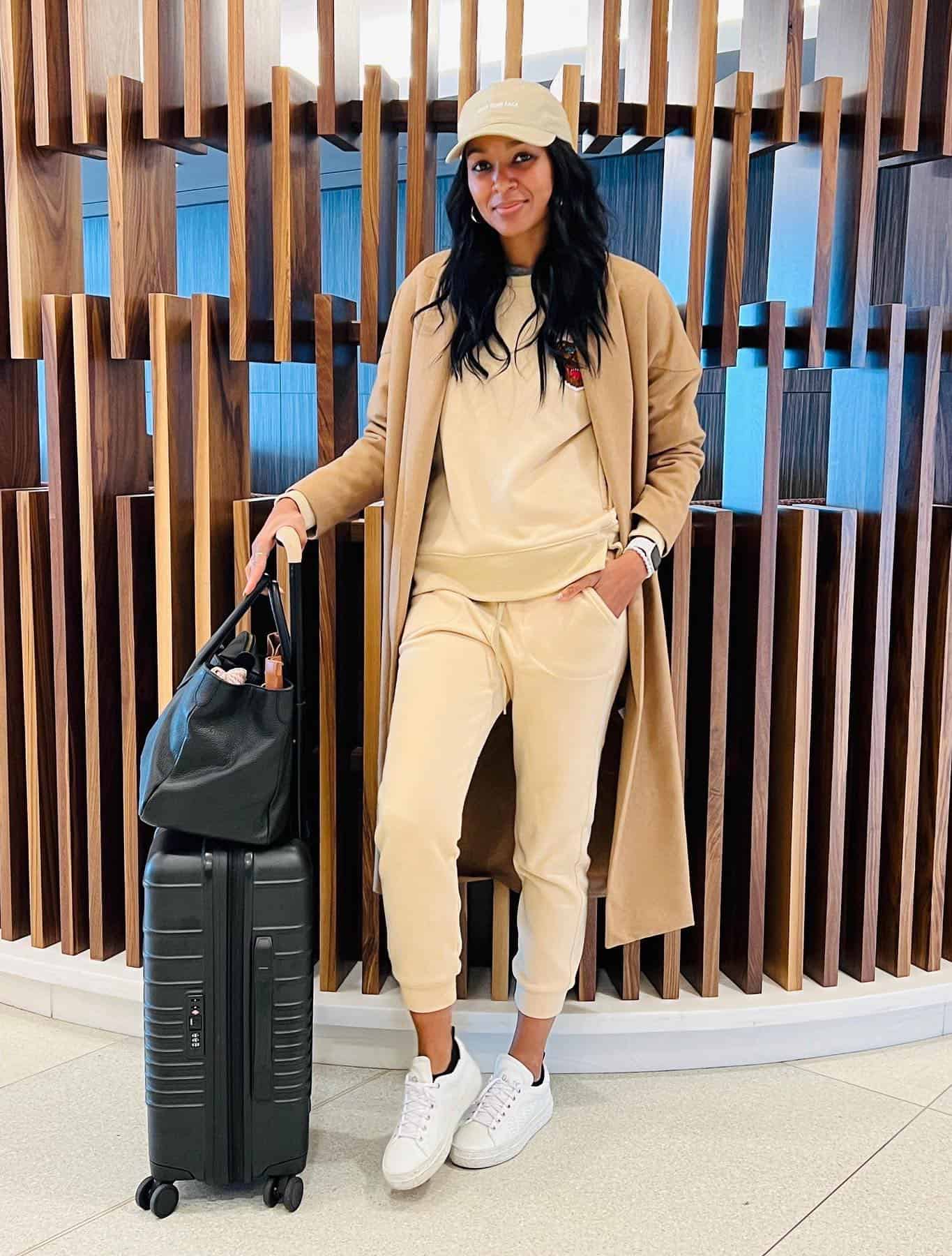 Woman wearing a tan matching lounge set with a tan coat and sneakers at the airport.